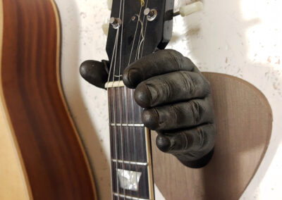 De hand met gitaar als houder aan de muur.